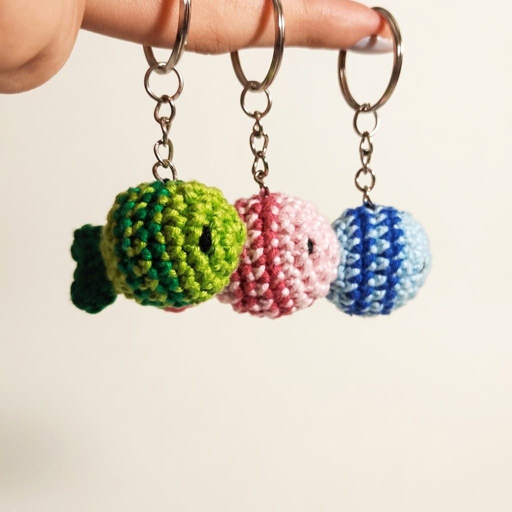 Três chaveiros de crochê em formato de peixinho, verde, rosa e azul